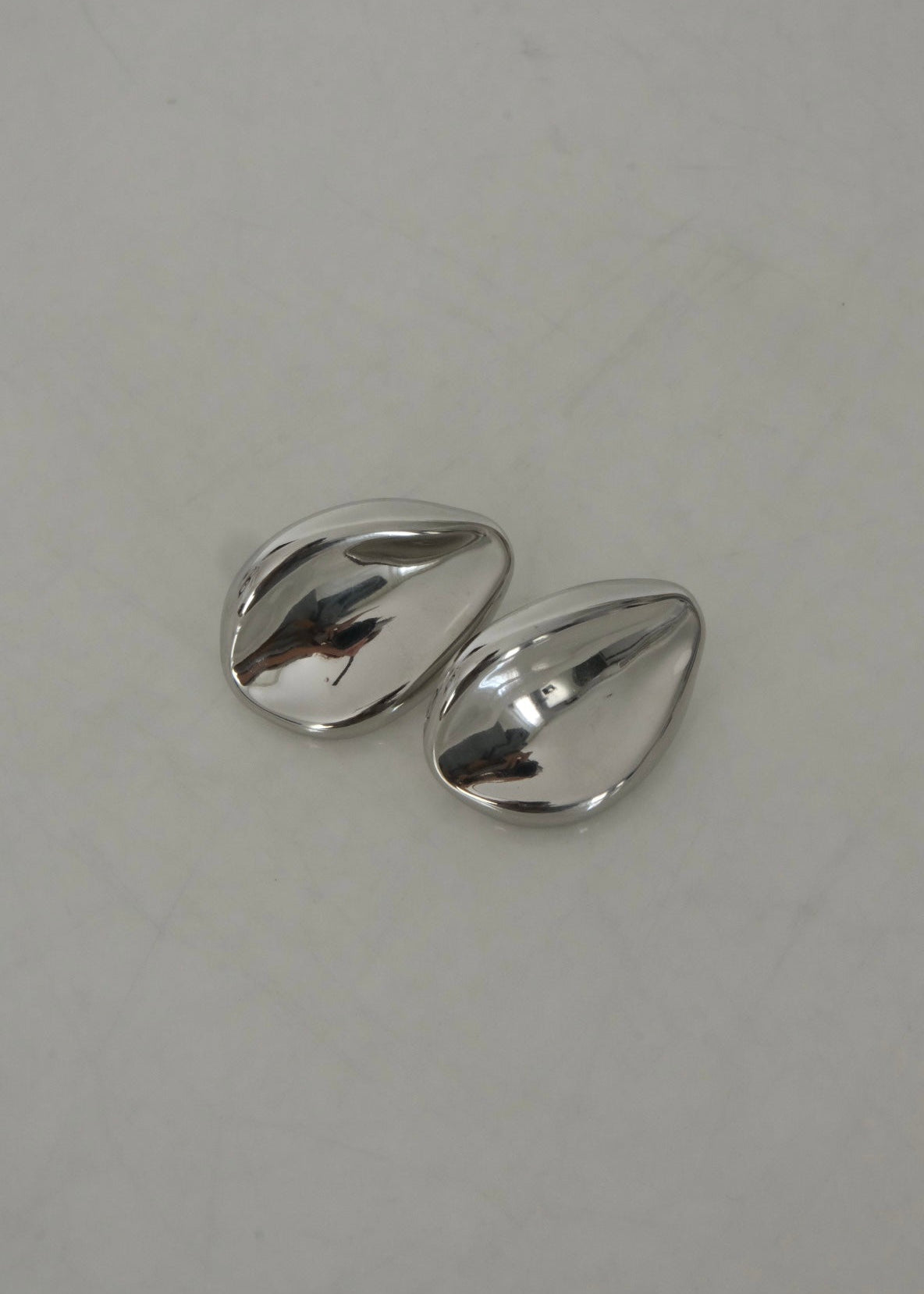 Boucles d’oreilles argentées en acier inoxydable au design organique, forme sculpturale et moderne, finition brillante.