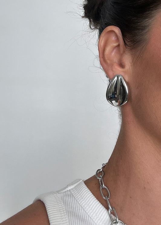 Boucles d’oreilles argentées en acier inoxydable au design organique, forme sculpturale et moderne, finition brillante.