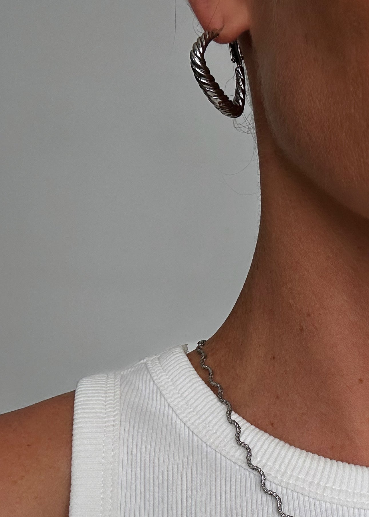 Créoles argentées en acier inoxydable, en forme de triangle torsadé, style moderne et géométrique.